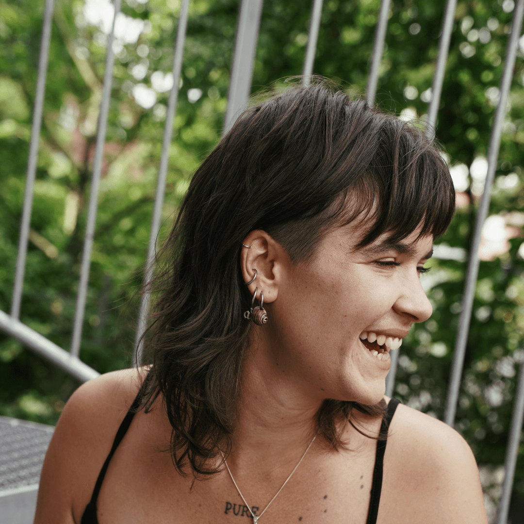 Noemi lächelt vor einem grünen Hintergrund zur Seite