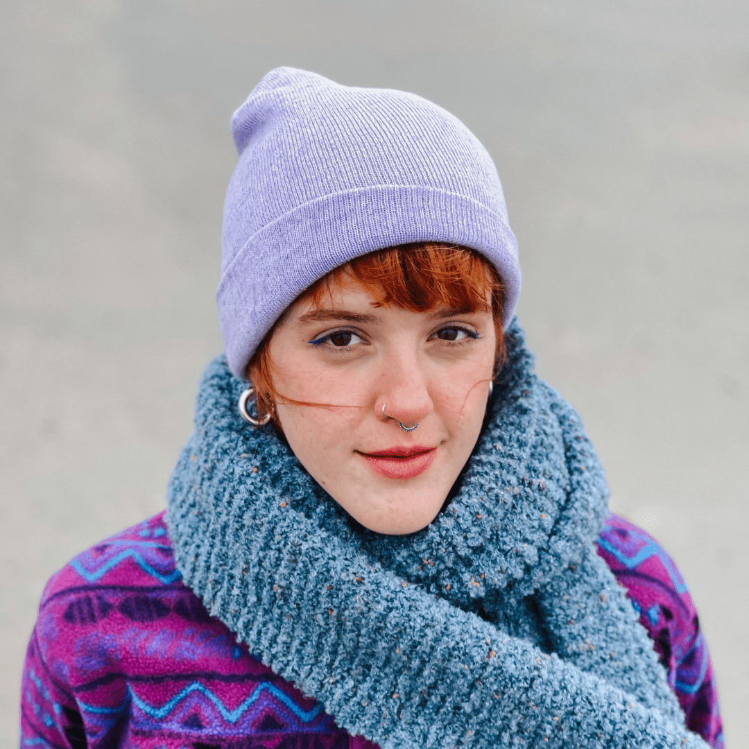 Georgia lächelt in die Kamera. Sie ist warm und farbenfroh eingepackt in eine violette Wollmütze, einen blauen Schal und eine lila Wolljacke